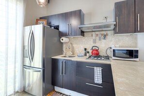 A compact kitchen with dark cabinets, a stainless steel refrigerator, a microwave, and a gas stove. - Charming & Sunlit Condo With Pool & Balcony - Near Golf, Beaches, & Nightlife (Cabo San Lucas)