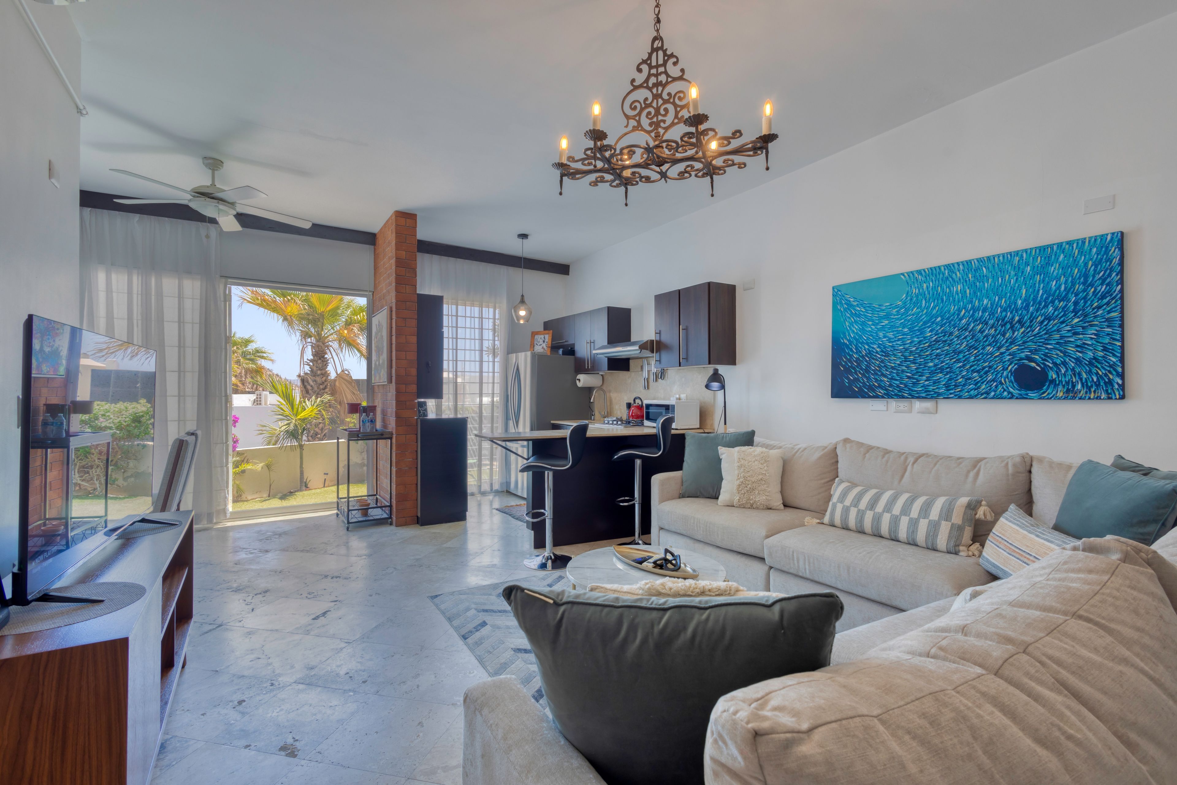 A modern living room with a sofa, a coffee table, and a TV. There is a kitchen area with cabinets and a dining table.