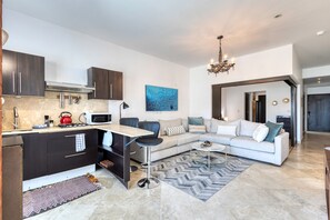 A modern kitchen with dark cabinets, a microwave, and a gas stove. There is a white sofa with cushions and a patterned rug in the living area. - Charming & Sunlit Condo With Pool & Balcony - Near Golf, Beaches, & Nightlife (Cabo San Lucas)