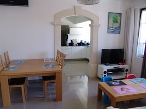 A dining area with a table and chairs, a television, and a kitchen in the background. - Well-equipped 8-person house with very large swimming pool. very close to town center. (Nîmes)