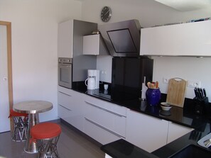 A modern kitchen with a built-in oven, coffee maker, and a clock on the wall. - Well-equipped 8-person house with very large swimming pool. very close to town center. (Nîmes)