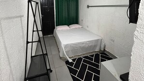 Una habitación pequeña y estrecha con cama, escritorio, silla, escalera y cortina verde.