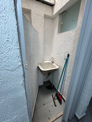 Een kleine badkamer met een wastafel, een bezem en een dweil die tegen de muur staat.