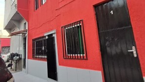 Un edificio rojo con una puerta negra, una ventana con barrotes y el número '1' visible en la puerta.