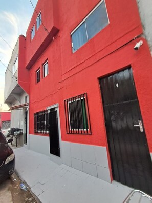 Un bâtiment rouge avec une porte noire, une fenêtre grillagée et un numéro « 1 » bien visible sur la porte.
