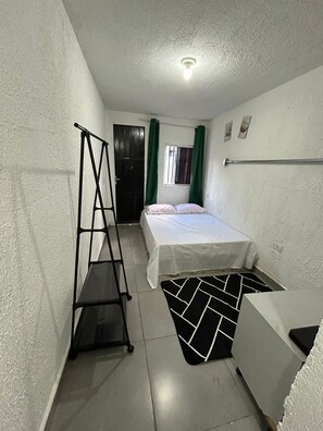 Een kleine, compacte kamer met een bed, een stoel, een trapje en een raam met gordijnen.