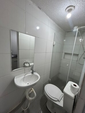 Une petite salle de bain compacte avec un lavabo blanc, un miroir, des toilettes et une douche.
