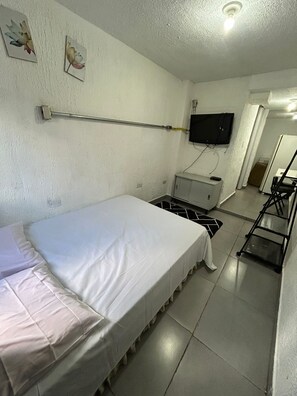 Een kleine, schone kamer met een bed, een aan de muur bevestigde televisie, een bureau en een stoel.