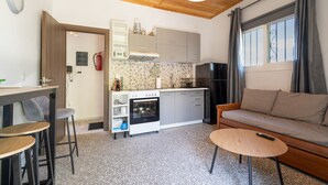 A compact kitchen with a built-in oven, a dining area with stools, and a sofa with a remote control on it. - Apartment 'Anna's House B' with Mountain View, Wi-Fi and Air Conditioning (Chortata)