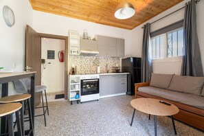 A compact kitchen with a built-in oven, a dining area with stools, and a sofa with a remote control on it. - Apartment 'Anna's House B' with Mountain View, Wi-Fi and Air Conditioning (Chortata)