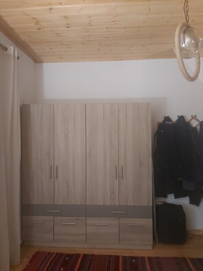 Ein Zimmer mit einem Holzschrank, einer Pendelleuchte und einem Kleiderständer mit Jacken.