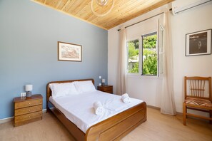 A bedroom with a wooden bed, a nightstand, a chair, a window with curtains, and a framed picture on the wall. - Apartment 'Anna's House B' with Mountain View, Wi-Fi and Air Conditioning (Chortata)