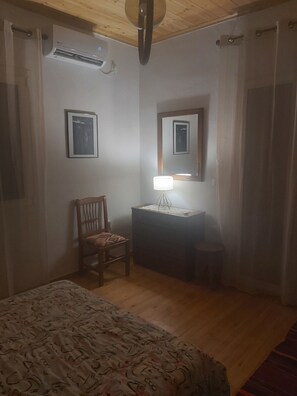Et soveværelse med en seng, et skrivebord med lampe, en stol og en klimaanlæg.