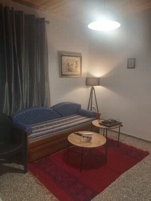 Een kamer met een bank, een klein tafeltje met een lamp, een ingelijst schilderij aan de muur en een rood vloerkleed.