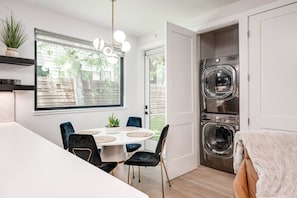 Eine moderne Küche mit Essbereich, integrierter Waschmaschine und Trockner sowie ein großes Fenster mit Blick ins Freie.