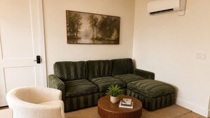 Una sala de estar con un sofá verde, un sillón blanco y una mesa de centro redonda con una planta.