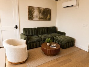 Ein Wohnzimmer mit einem grünen Sofa, einem weißen Sessel und einem runden Couchtisch mit einer Pflanze.