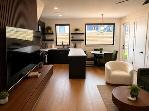 A modern kitchen with a central island, a dining area with a round table, and a seating arrangement. - Rooftop Lounge ATX I 2 Fire Pits + Outdoor TV (Austin)