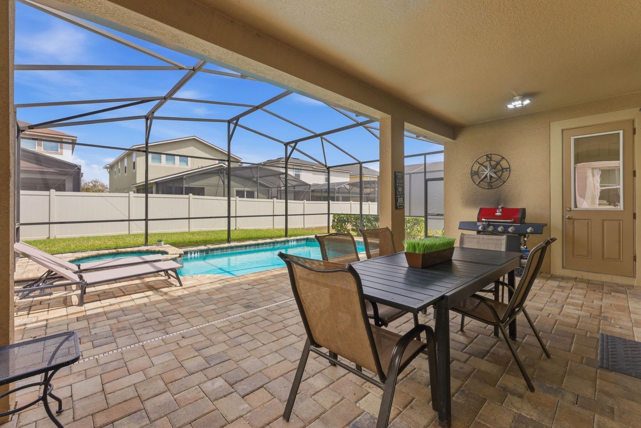Un patio couvert avec une piscine, des sièges d’extérieur et un barbecue.
