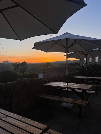 An outdoor patio with wooden tables and umbrellas, overlooking a sunset.. The Wheatsheaf