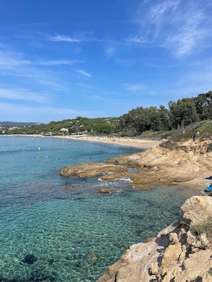 Paisatge costaner amb aigua cristal·lina, un litoral rocos i una platja allunyada.