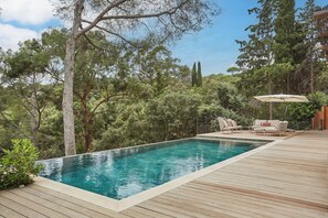 Una piscina con cubierta de madera, rodeada de árboles y un área de descanso con toldo.