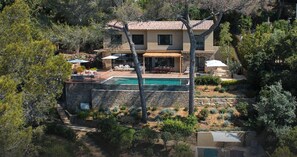 Una casa de dos pisos con piscina, mobiliario exterior y un muro de piedra.