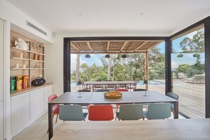 Un comedor con una mesa y sillas, un estante de madera con libros y vistas al exterior.