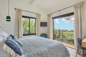 Un dormitorio con una cama grande, televisión, balcón con vista a la vegetación y una silla.