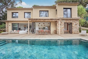 Una casa moderna amb piscina, zona de menjador a l'exterior i un mur de pedra.