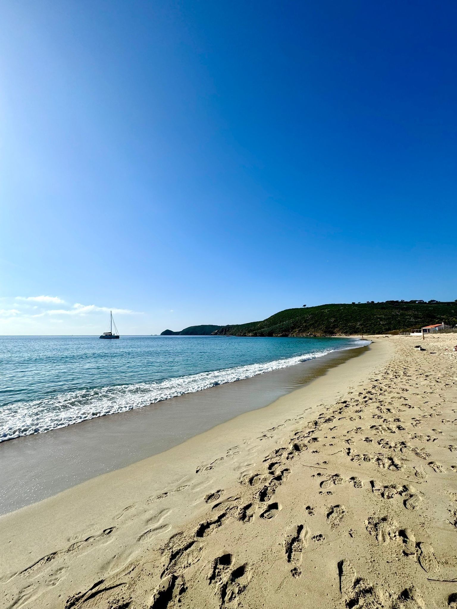 Ein Strand mit Fußabdrücken, einem Segelboot und einem Gebäude in der Ferne.