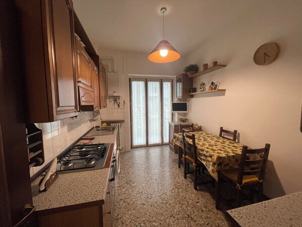 Una cucina con piano cottura a gas, mobili in legno, un tavolo da pranzo con sedie, una lampada a sospensione e un orologio appeso al muro.