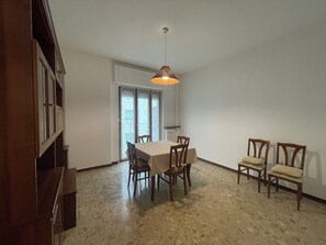 Zona pranzo con tavolo e sedie, una lampada a sospensione e una porta scorrevole in vetro che dà su uno spazio esterno.