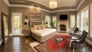 A bedroom with a large bed, a fireplace, a TV, and a view of the outdoors. - Grand Luxury 11,000 sq ft Estate — 6BR, 8BA, Pool & Premium Finishes (Dallas)
