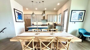 A modern kitchen with white cabinets, a wooden dining table, and pendant lights. - La-La-Lakeshore - Lake Front, Boat Dock & Launch (Spicewood)
