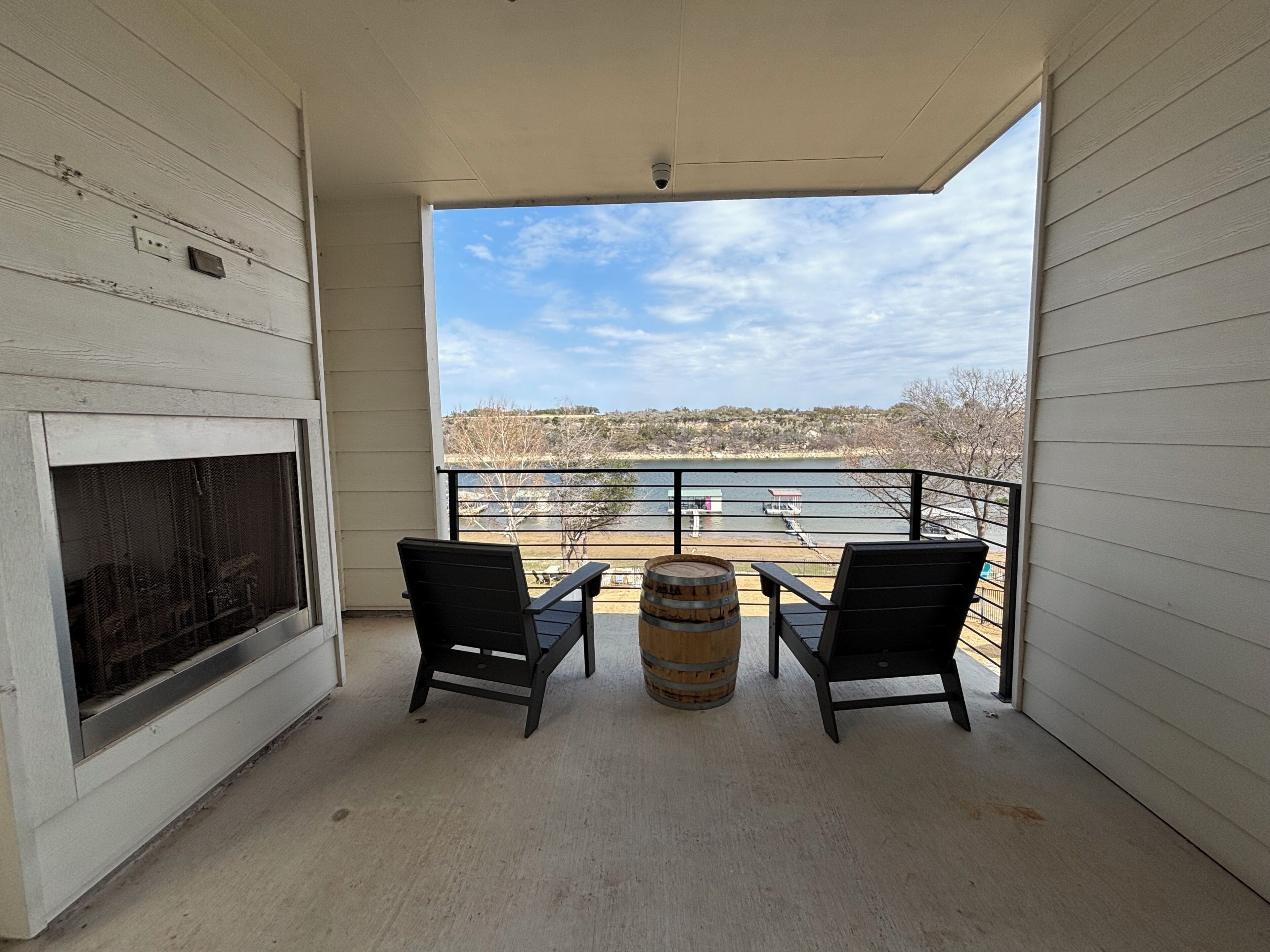 A balcony with two chairs and a barrel, overlooking a body of water and distant landscape.