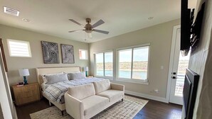 A bedroom with a bed, a white sofa, a ceiling fan, and a view of the outdoors. - La-La-Lakeshore - Lake Front, Boat Dock & Launch (Spicewood)