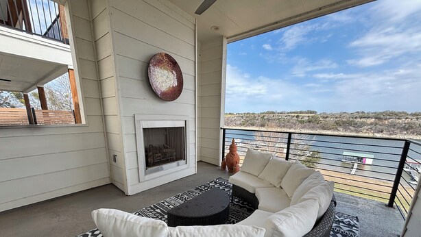 A balcony with a white sofa, a fireplace, and a view of the landscape. - La-La-Lakeshore - Lake Front, Boat Dock & Launch (Spicewood)
