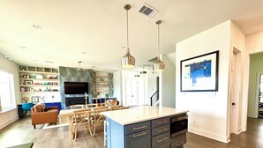 A modern kitchen with a central island, wooden dining table, and pendant lighting. - La-La-Lakeshore - Lake Front, Boat Dock & Launch (Spicewood)