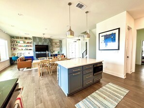 Eine moderne Küche mit Kochinsel, Esstisch aus Holz und Pendelleuchten.