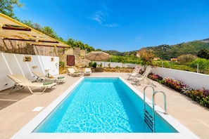 A rectangular swimming pool with clear blue water, surrounded by lounge chairs and a small table with an umbrella. - Villa Koupos in Kare (Rethymno)