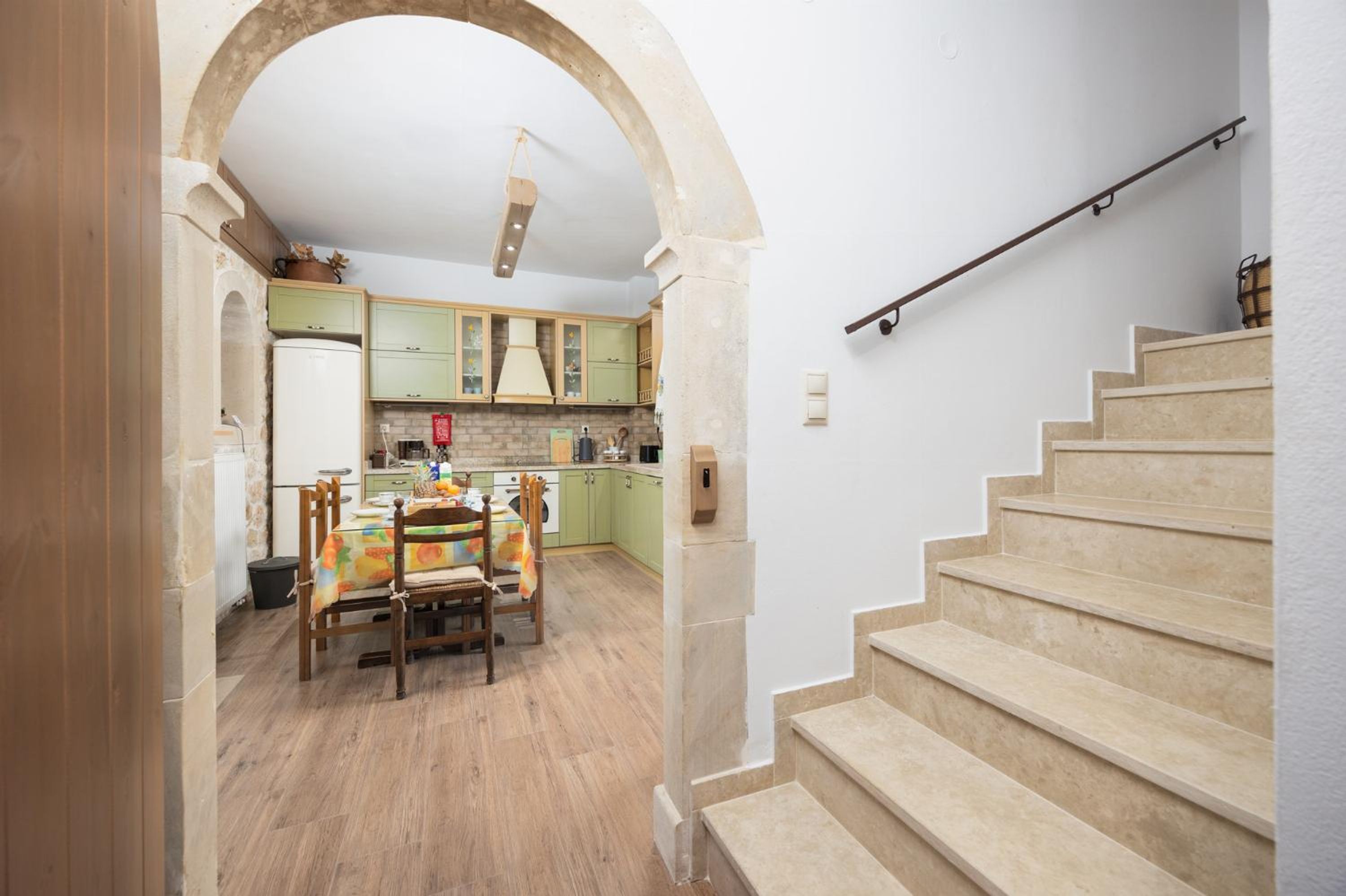 A kitchen with a dining table and chairs, a staircase, and a hallway with an archway.