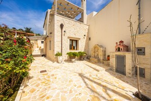 A stone courtyard with a building, a small structure with a red roof, and a tree. - Villa Koupos in Kare (Rethymno)