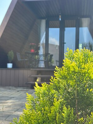 Uma casa moderna com fachada de madeira, porta de vidro e um pátio visível com mobiliário de exterior.