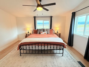 Une chambre à coucher comprenant un lit, deux lampes de chevet, un ventilateur de plafond, une fenêtre avec vue et une table de chevet.