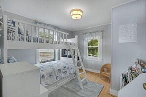 Quarto de criança com beliches, escada, estante e janela com vista.