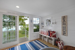 Una habitación con vista al agua, un banco con almohadones decorativos y un cartel en la pared que dice 'BEACH HOUSE'.