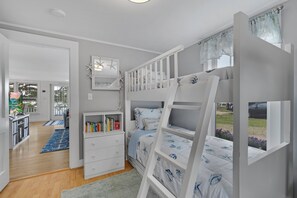 Quarto de criança com beliches, estante, escrivaninha e vista para o exterior.