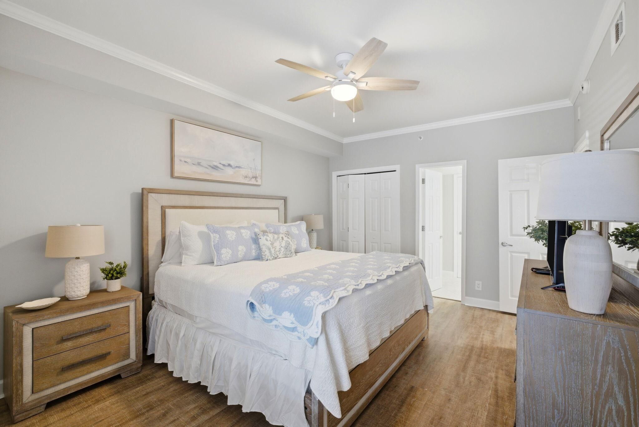 A bedroom with a bed, nightstand, dresser, ceiling fan, and a door.