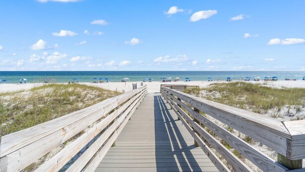 A wooden boardwalk leading to a beach with sand dunes and a clear blue sky. - Seaspray Riverside 112 (Pensacola)